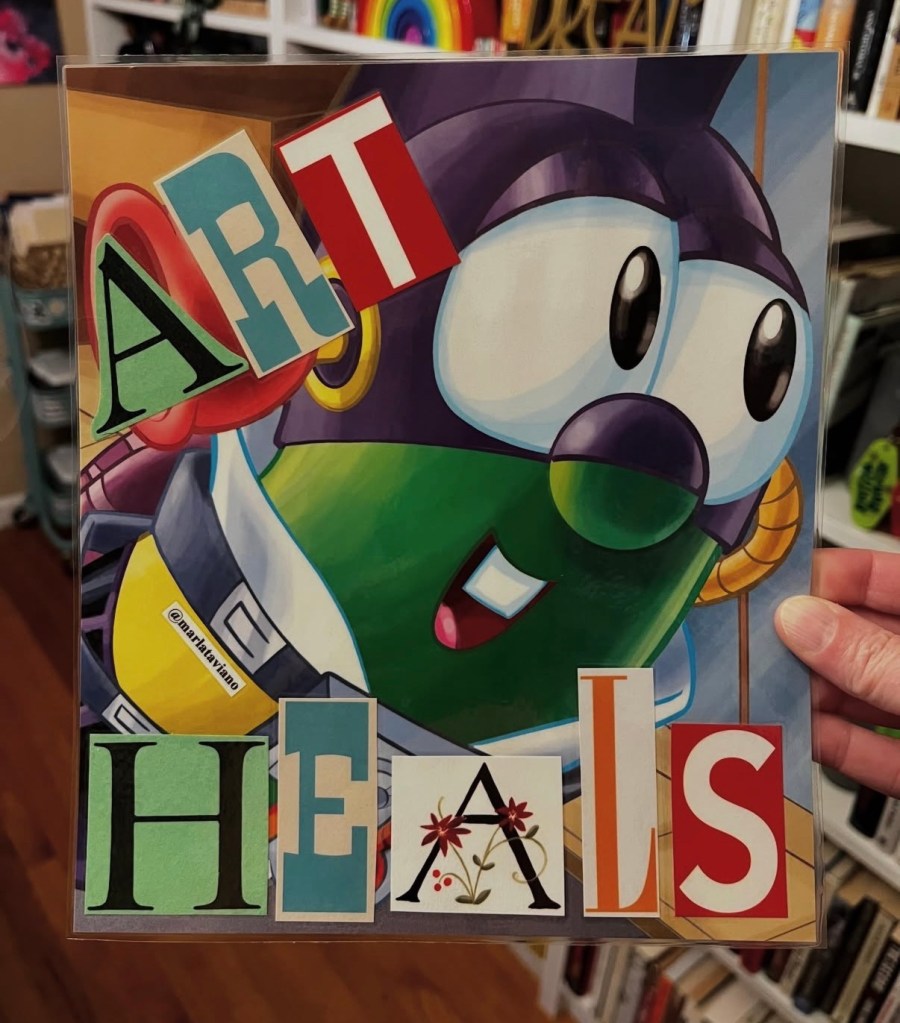 Hand-collaged word art on an illustrated page of a caped animated character, with large cutout letters spelling "ART" and "HEALS" across the piece. Marla Taviano's word art "art heals" glued onto the artwork.